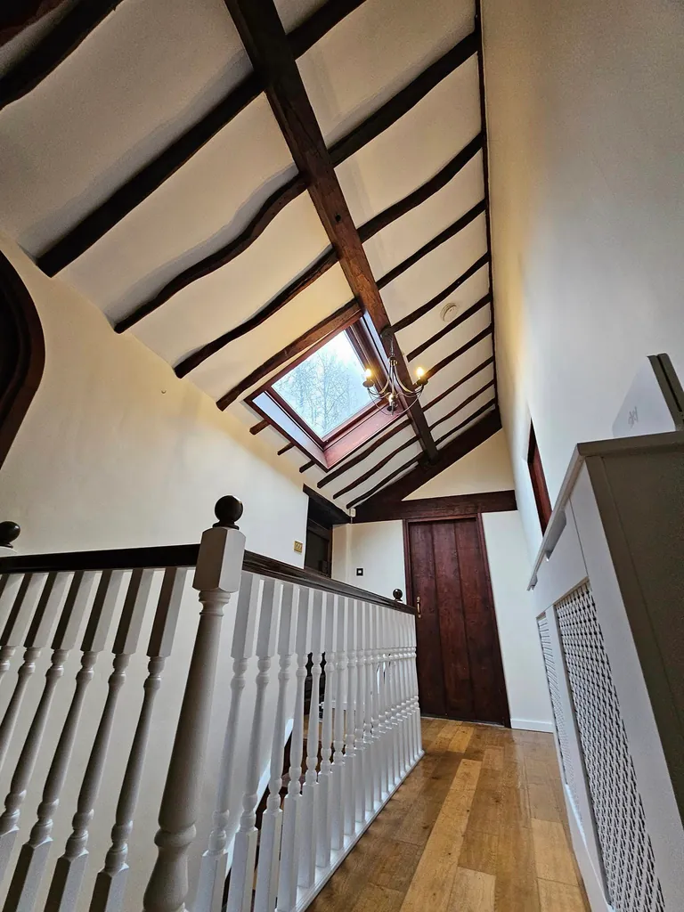 White-painted upstairs landing with exposed dark beams and a skylight