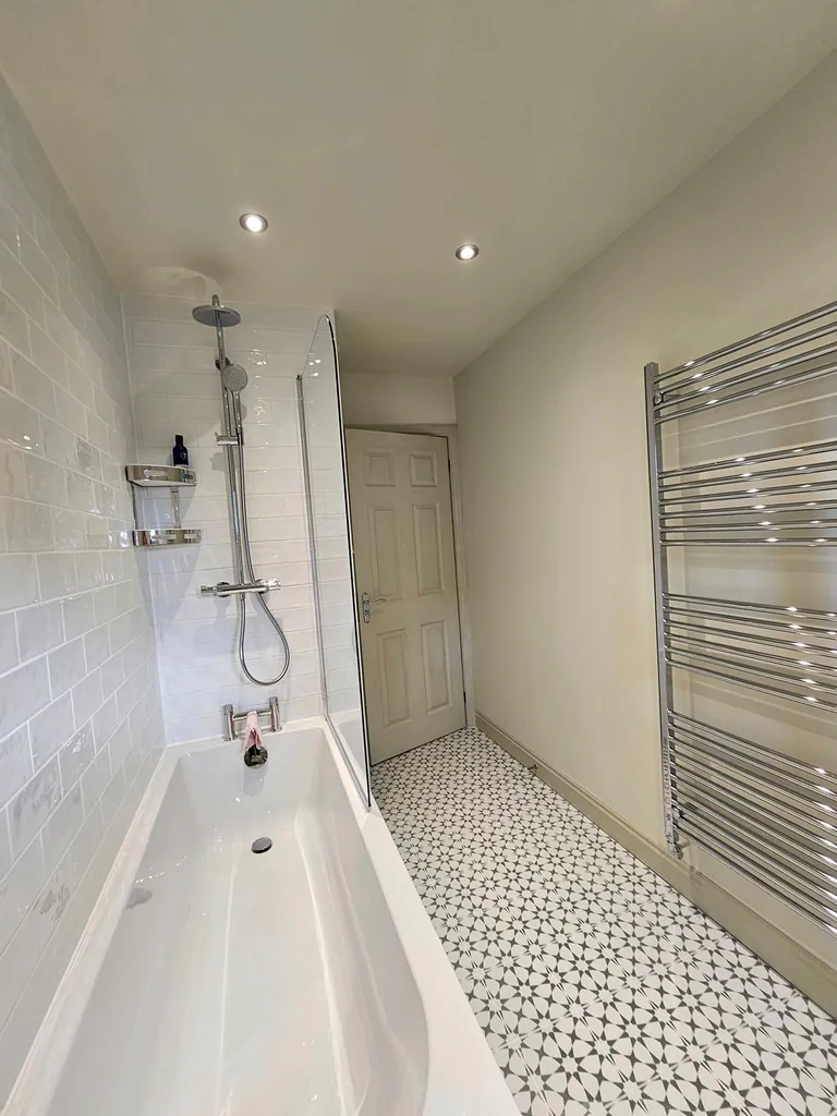 Bathroom with pale walls, a white bath and patterned floor tiles